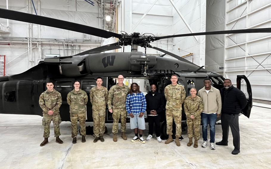 Airmen and football players pose for a picture in front of a Black Hawk helicopter