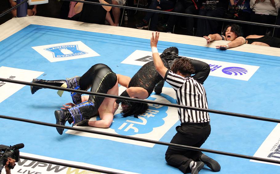 A referee observes two wrestlers on a mat.