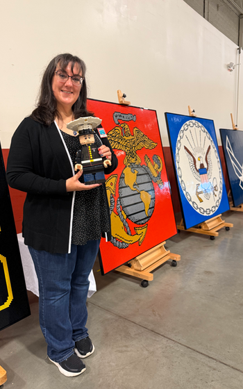 A woman holds a LEGO Marine and stands in front of a LEGO display.