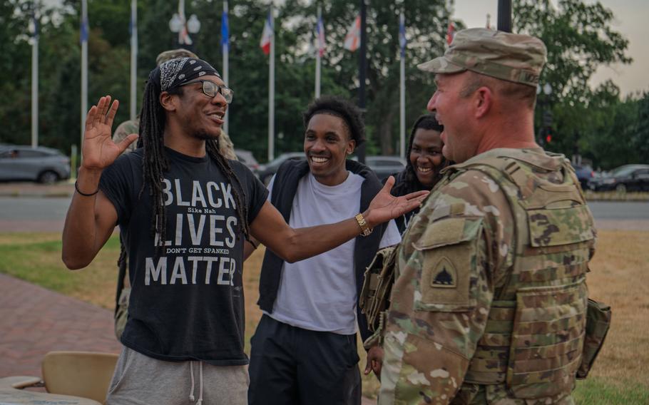 Three people and a soldier, all grinning or laughing; a second soldier is mostly obscured by one of the civilians.