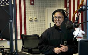 A sailor at a desk speaks into a microphone.