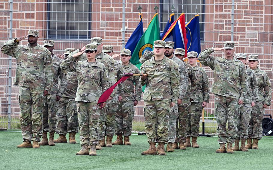 Troops salute in formation in front of a building.