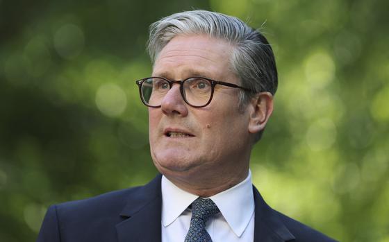 Close-up view of Keir Starmer, wearing a dark suit and glasses, standing in front of trees.