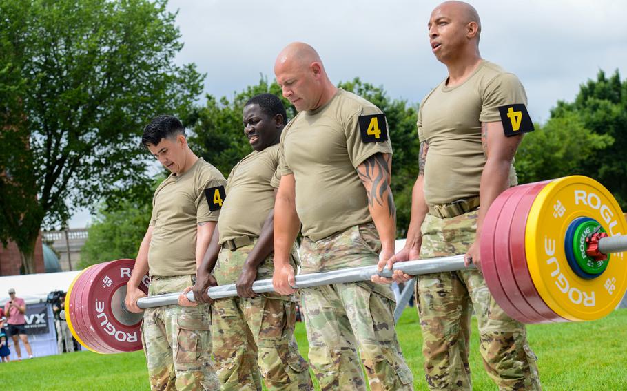 Four soldiers lift a barbell as a team.
