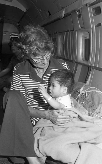 A woman holds an infant partially swaddled in a blanket.