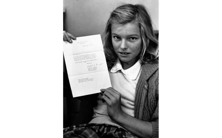 A vertical, black and white photo of a girl holding a letter with two hands.
