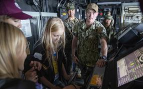 Seaman William Hube explains the steering of the amphibious transport dock ship USS Arlington to a group of Ukrainian children during a port visit in Riga, Latvia, in 2022. Sailors proficient in certain languages, including Ukrainian and Latvian, can earn a $500 bonus by qualifying under a Navy testing program outlined in an April 24 memo. 