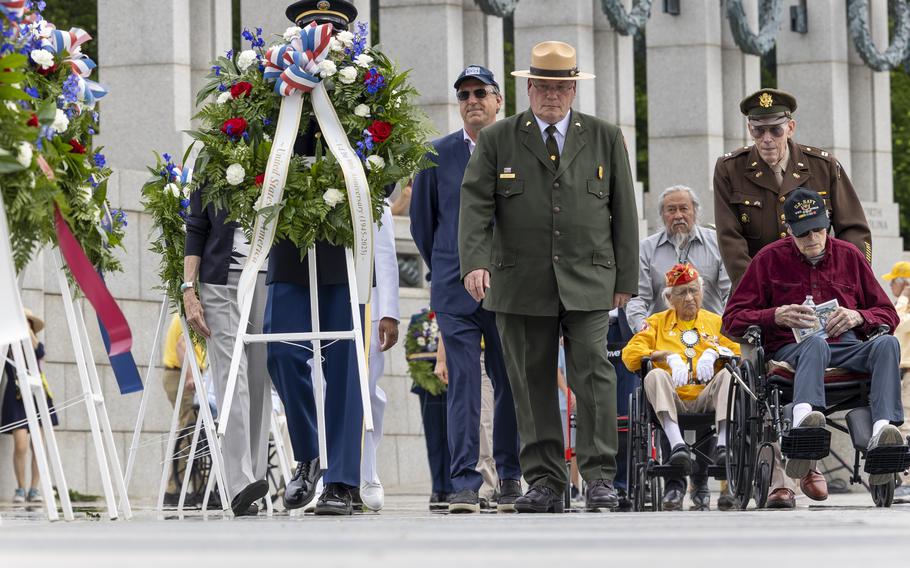 A group of men walk along the memorial with others in wheelchairs as wreaths are positioned in front of them.