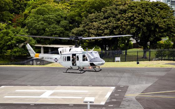 A white U.S. Air Force helicopter sits on a marked helicopter landing pad surrounded by lush green trees.