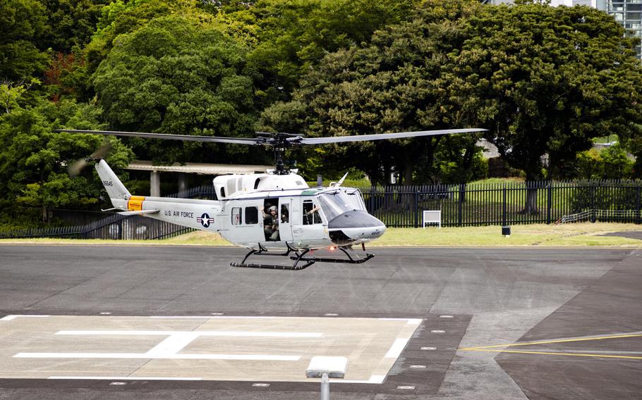 A white U.S. Air Force helicopter sits on a marked helicopter landing pad surrounded by lush green trees.