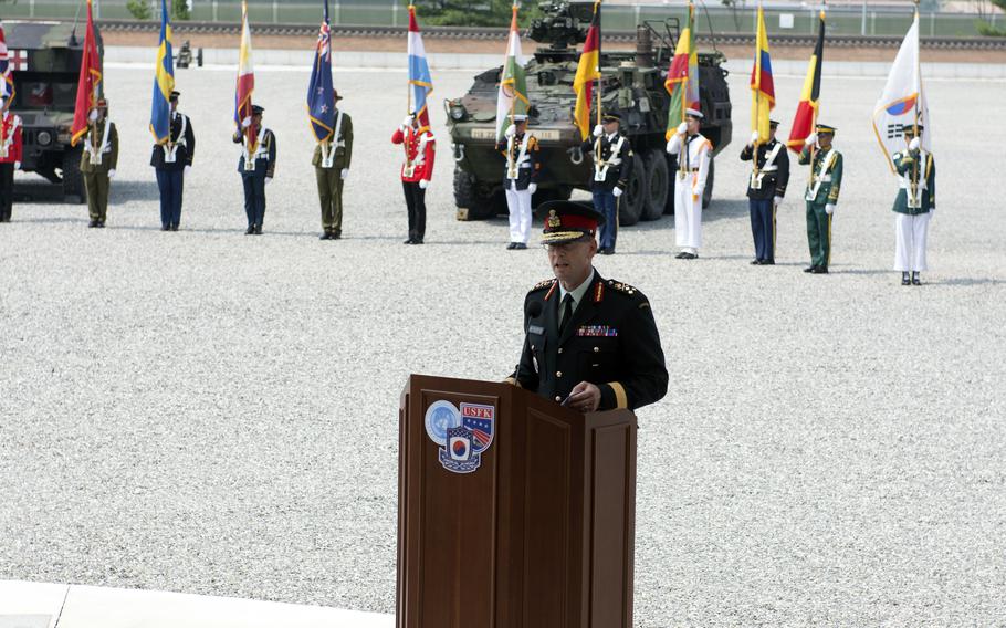 U.N. Command’s deputy commander speaks at a podium while service members carrying member nation flags line up behind him.