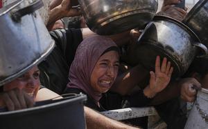 Palestinians struggle to hold out bowls to receive aid.