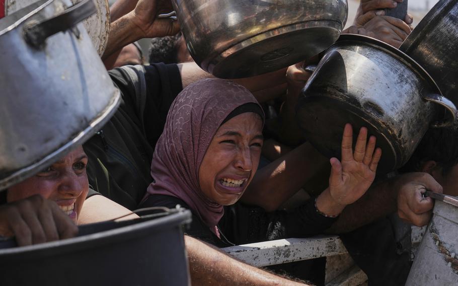 Palestinians struggle to hold out bowls to receive aid.