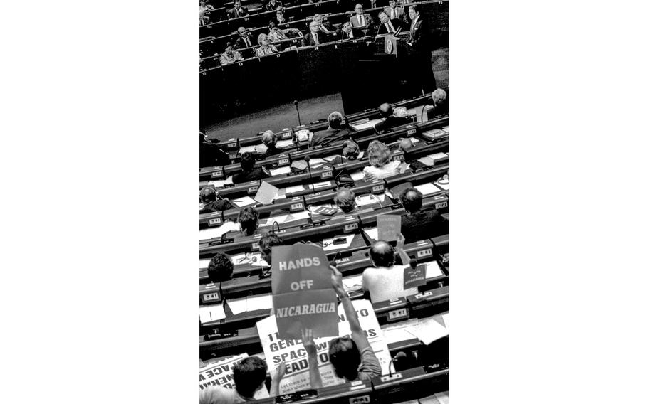 Strasbourg, France, May 1985: As President Ronald Reagan (top right) speaks to the European Parliament, members of the group hold up signs protesting nuclear weapons and U.S. policy in Central America.