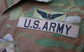 A close-up view of a badge reading “U.S. Army” on a camouflage uniform.