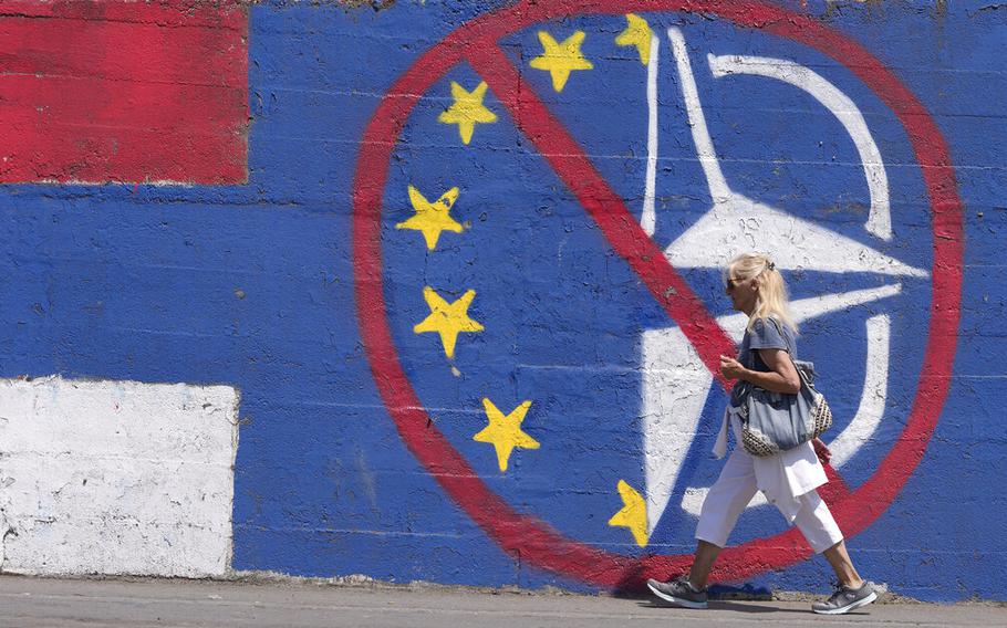 A woman walks by a wall in Belgrade, Serbia, Tuesday, June 21, 2022, that shows the colors of the Serbian flag and graffiti against EU and NATO.  European Union leaders will seek to offer support this week to six Western Balkan nations that have long been knocking at the bloc’s doors.