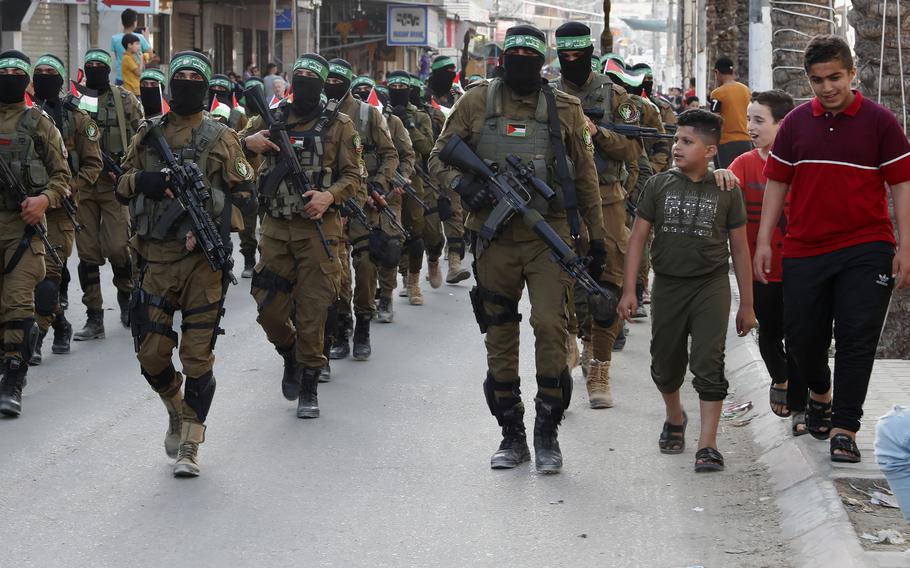 Children talk with masked militants from the Izzedine al-Qassam Brigades, a military wing of Hamas, hold their national flags while marching along the streets of Nusseirat refugee camp, central Gaza Strip, on May 28, 2021. Arabic on the headband reads “No God but Allah and Muhammed is his messenger, al-Qassam Brigades.”