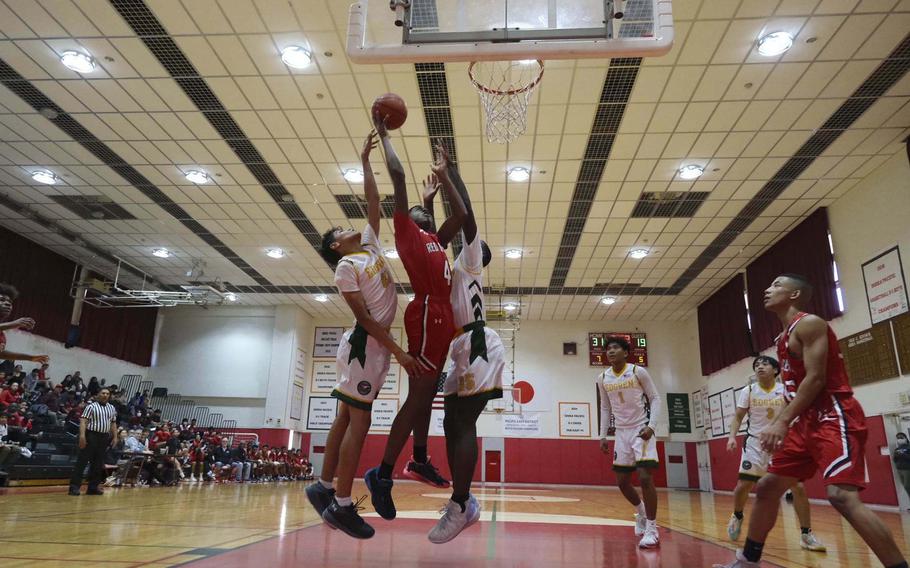 Nile C. Kinnick's Austin Davenport skies for a rebound against Robert D. Edgren's Noah Medonis and O'moj Reeves during Saturday's DODEA-Japan boys basketball game. The Red Devils won 64-26.