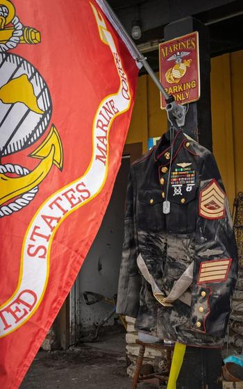 Dirty Marine Corps uniform hangs alongside a Marine Corps flag.