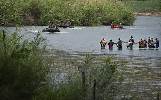 Migrants, including families with small children, join hands to fight the current as they wade across the Rio Grande near the Eagle Pass-Piedras Negras International Bridge on August 12, 2022 in Eagle Pass, Texas. Texas National Guard look on as they people make their way across. They will turn themselves into Border Patrol and be transported to a nearby government processing center. MUST CREDIT: Washington Post photo by Sarah L. Voisin.