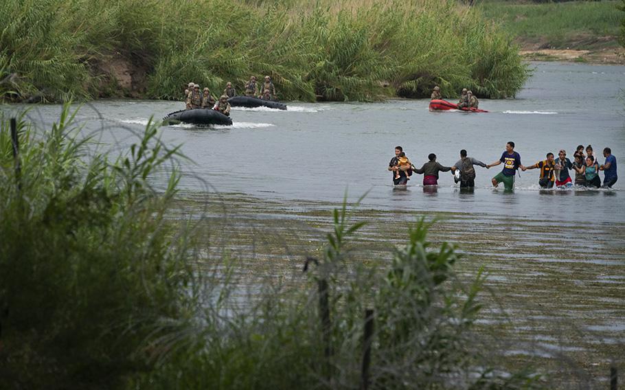 Migrants join hands as they wade across the Rio Grande near the Eagle Pass-Piedras Negras International Bridge on August 12, 2022 in Eagle Pass, Texas, as National Guard members look on.