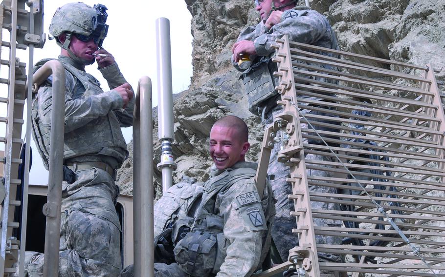 Soldiers chatting, two standing and one sitting and grinning.