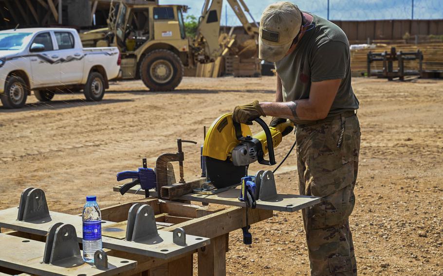 A soldier in camouflage pants and a green t-shirt uses a circular saw on a construction site. 