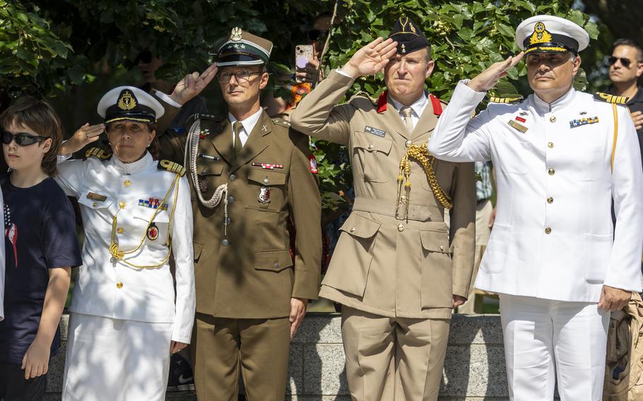 Four people in white and khaki military suits salute.