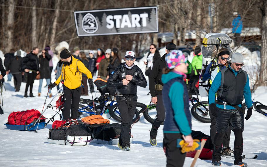 Air Force Maj. Joshua Brown, dressed in black jacket and pants, walks amid fellow participants as the Iditarod Trail Invitational kicks off at Knik Lake, Alaska, Feb. 27, 2022.
