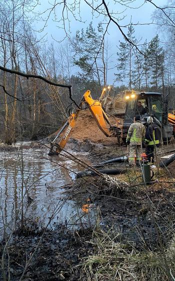 Recovery equipment seen clearing mud from a distance while two emergency workers stand near it.