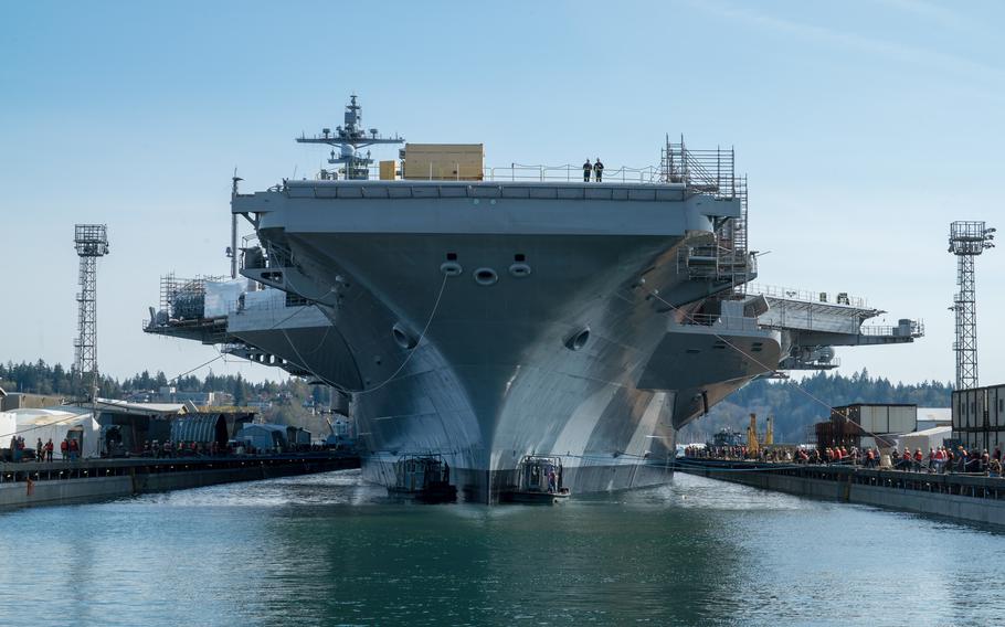 An aircraft carrier, seen from the front at a low angle, sits in a berth in dry dock.