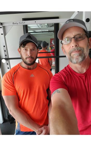Two men in baseball caps and T-shirts pose for a photo with a mirror behind them.