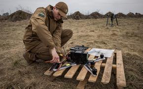 A man kneels over a drone in a field.