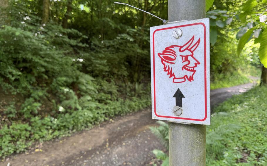 A placard featuring a red devil figure is nailed to a post in the woods.