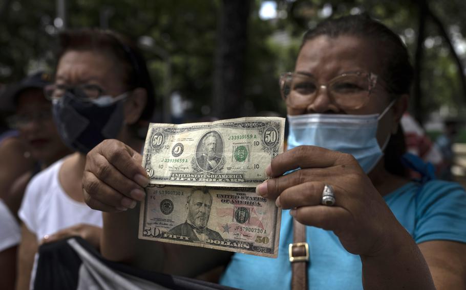 A woman holds up dollar bills to show that she wants to be paid in U.S. currency, during protests of active and retired public workers demanding the government pay their full benefits in Caracas, Venezuela, Tuesday, Sept. 6, 2022. As the value of the U.S. dollar soars, other currencies around the world are sinking by comparison.