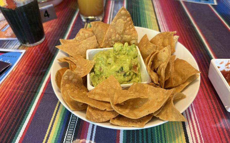 A plate of tortilla chips with guacamole and salsa sits on a colorful tablecloth.