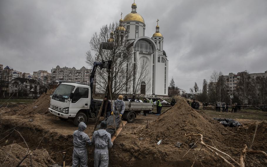 Workers in protective gear exhume the bodies of civilians found buried in a mass grave behind a church on April 13, 2022.