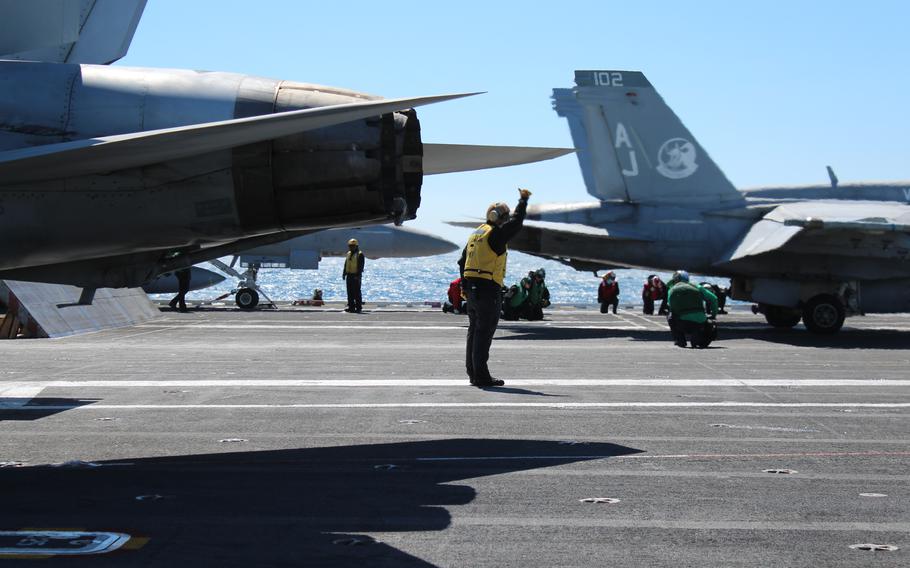 A crew member stands on the ship’s deck surrounded by fighter jets.