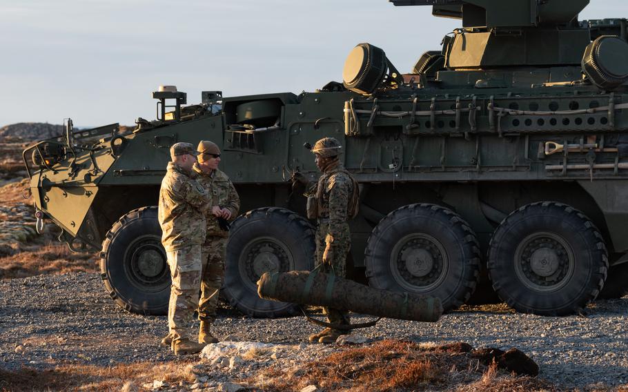 Two soldiers speak, standing in front of the missile defense system.