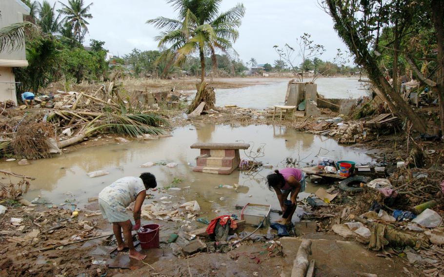 A Philippine woman and young girl wash clothes in the muddy water where a house was destroyed; only its front step remains.