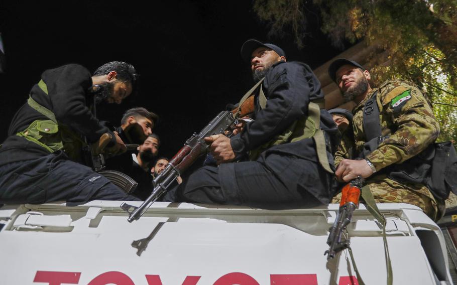 Security forces in blue and camouflage uniforms holding assault weapons sit in the back of a pickup truck.