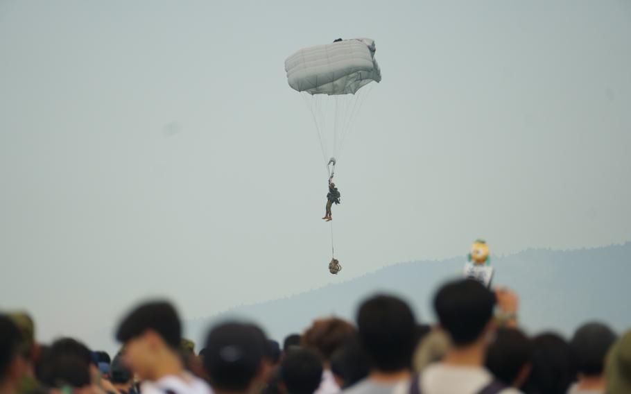 A Japan Ground Self-Defense Force soldier parachutes to the ground in front of a crowd of spectators.
