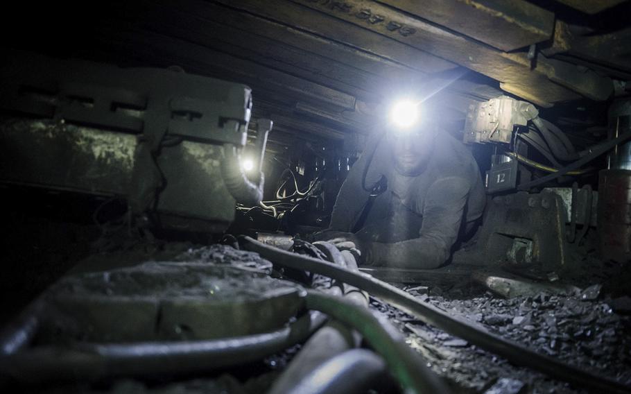 A miner operates an excavator in a cramped corridor deep underground. 