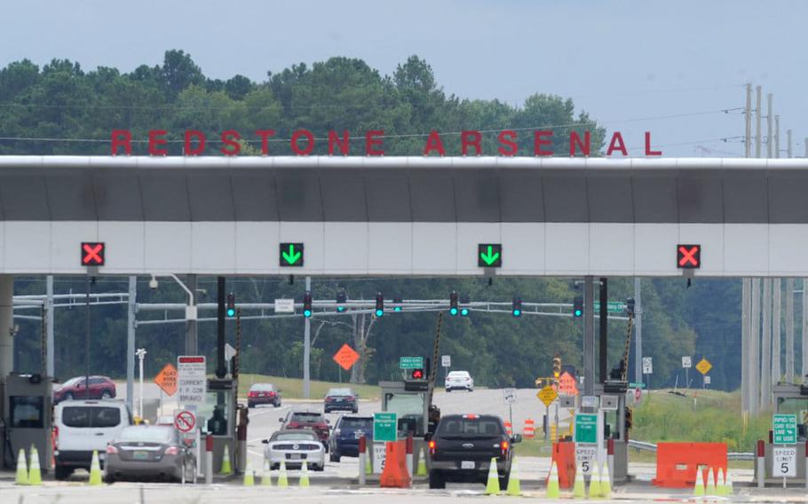 Cars stop at a multi-lane gate, with “Redstone Arsenal” in standing letters on the roof of the gate.