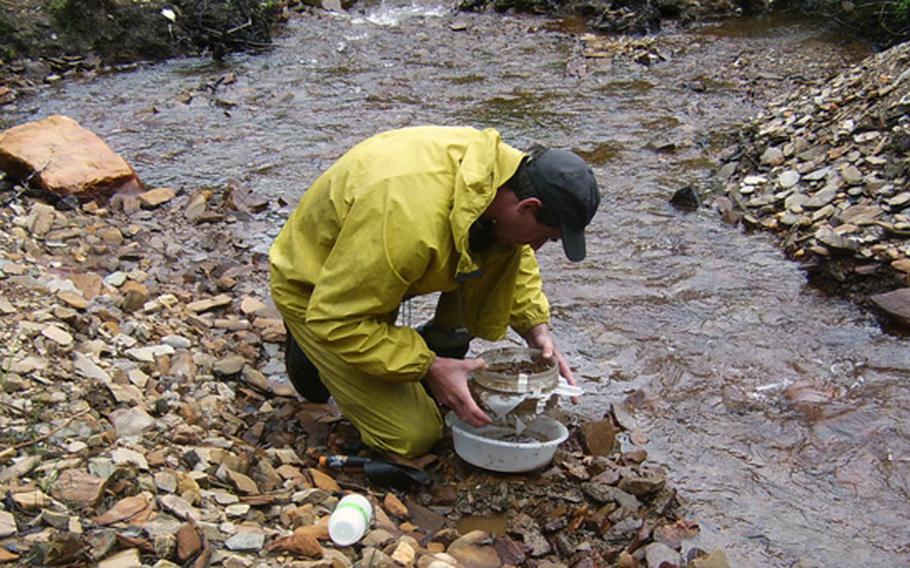 A man collects sediment in a stream bed.