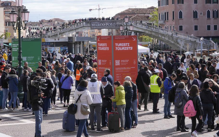 Stewards check tourists QR code access outside the main train station in Venice, Italy, Thursday, April 25, 2024. 