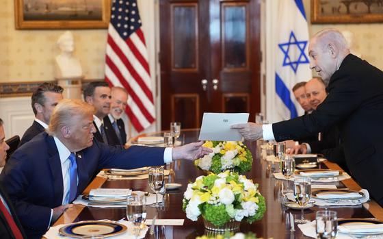 Benjamin Netanyahu hands Donald Trump a folder across a large conference table with other officials seated behind them at place settings.