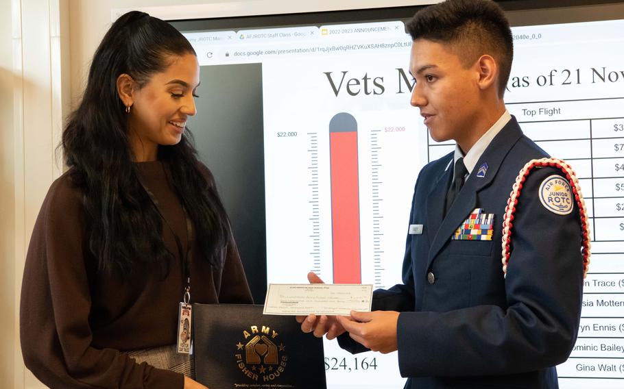 Cadet commander Philip Stacey, right, presents a check to Landstuhl Fisher House manager Sarafina Buchanan at Kaiserslautern High School, Germany, Nov. 21, 2022. 