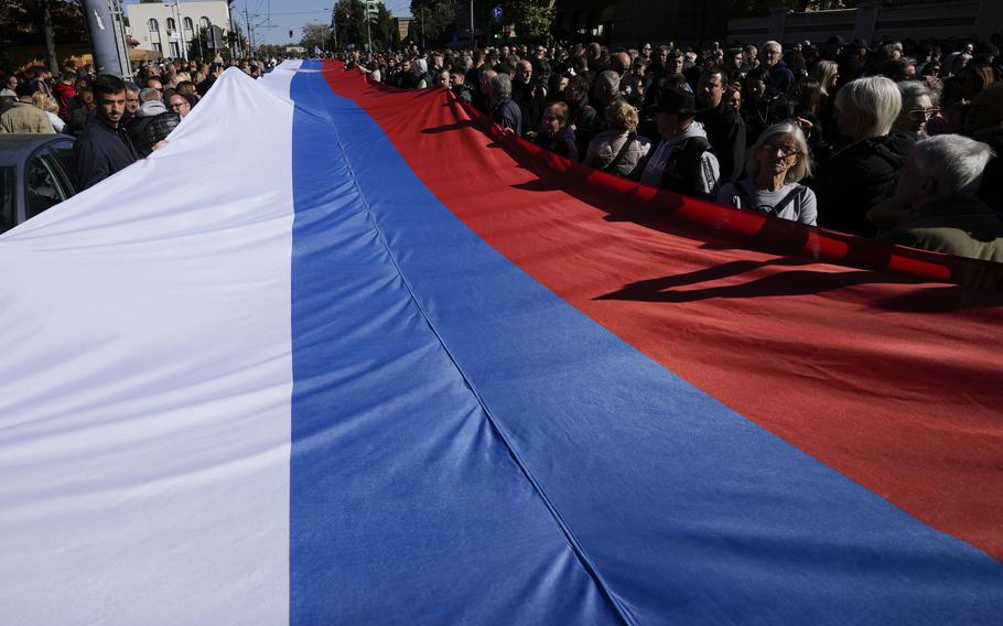 A mass of people hold a large three-color flag.