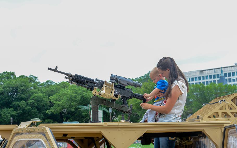 A woman and a child sit atop a military vehicle gripping a machine gun.